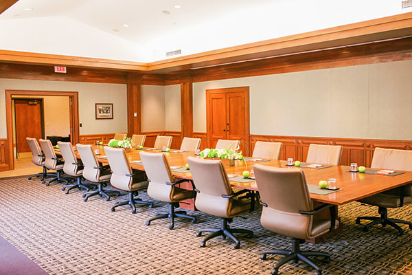 A modern conference room with a large wooden table surrounded by executive chairs, featuring green accents and natural lighting.