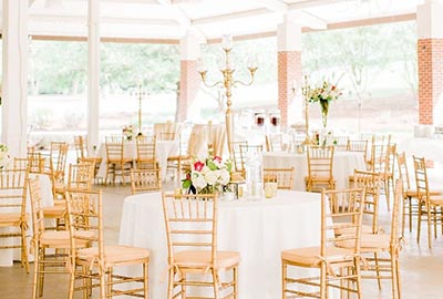 Elegant banquet hall setup with round tables adorned with floral centerpieces and golden chairs.