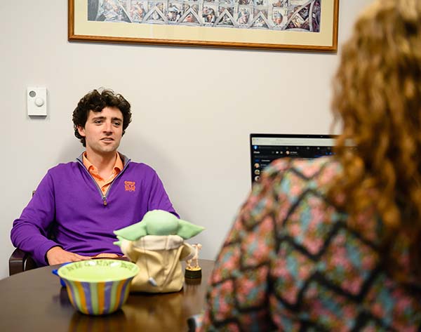 Grant Wilkins sitting in a chair and talking to Robyn Curtis, who is seated at her desk.