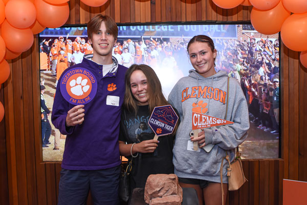 Three admitted students pose with a replica of howards rock while holding Clemson themed props and signs