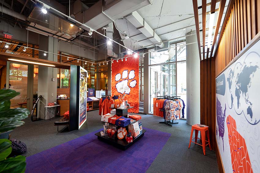 A mannequin with Clemson apparel and a rack of Clemson hats in the retail space at Experience Clemson.