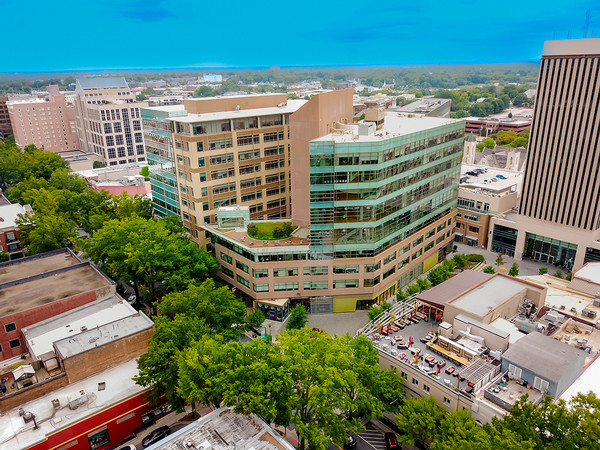 Aerial view of a modern glass office building surrounded by downtown structures and greenery.