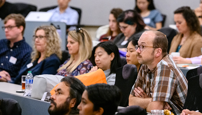 A room full of new faculty sit at their desks as they attend a conference.