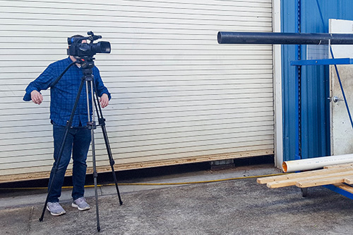 Videographer positioning camera outside of a garage door with construction materials nearby.