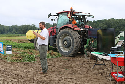 Speaker presenting in front of a tractor in a field.