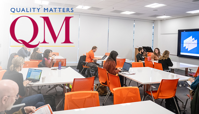 Instructors meeting in a classroom with the QM logo in the upper left corner