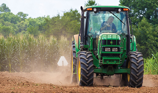 Tractor tilling soil corn crop in background.