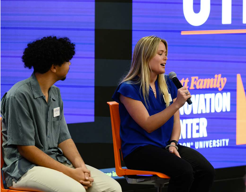 two students sitting on a stage, one with a mic