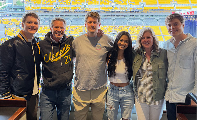 The Guskiewicz family dressed in casual attire pose at a stadium for a sporting event.