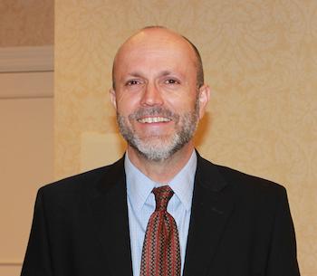 Portrait of a smiling man in a suit and tie, standing in a formal setting.