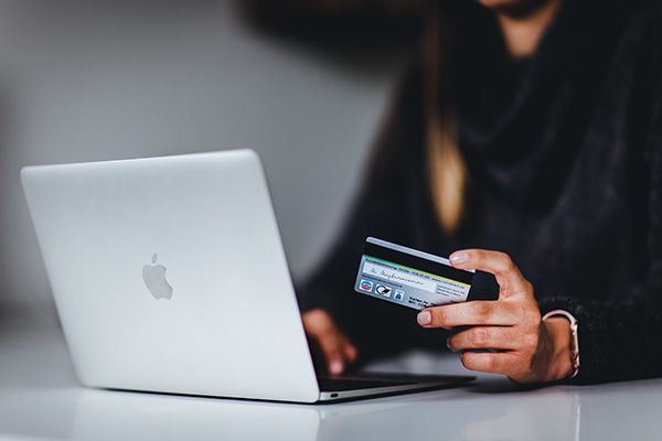 Person holding out their credit card while typing on a laptop