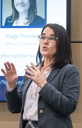 A professional woman with glasses gestures while speaking.