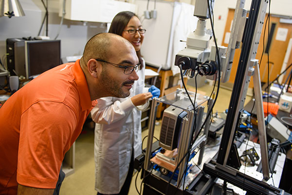 Two researchers, one male and one female, are engaged in a hands-on experiment in a laboratory setting, with various scientific equipment visible around them.