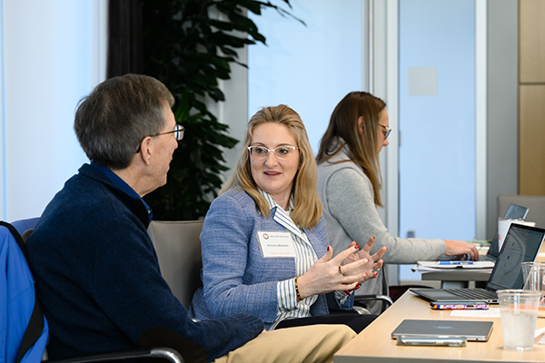 Two departmental chairs engage in a discussion at a conference table, while another colleague works on a laptop in the background.