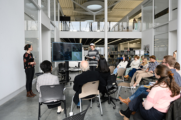 A group of students attending a landscape architecture review in Lee Hall, with another student presenting on a large screen.