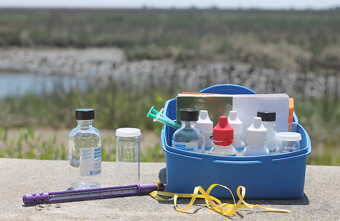 A dissolved oxygen testing kit and thermometer with a marsh view in the background.