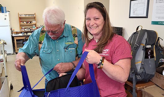 Trainers Jack and Beth opening SC Adopt-a-Stream tote bags. Jack is looking into a bag while Beth is smiling.