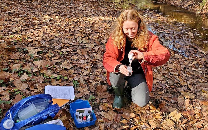 Trainer Haley kneeling next to a stream while beginning a dissolved oxygen test.