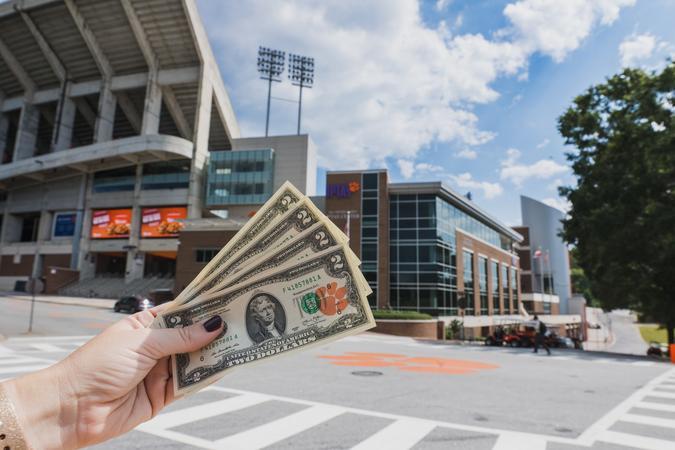 female showing dollar bills against university campus background