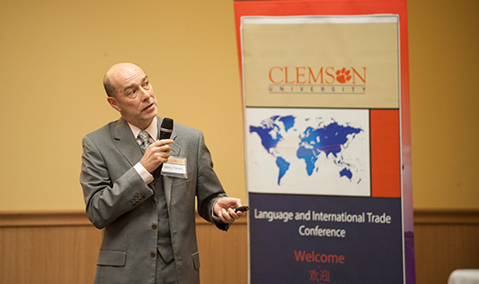 A male presenter pointing to a screen with a poster of world map next to him