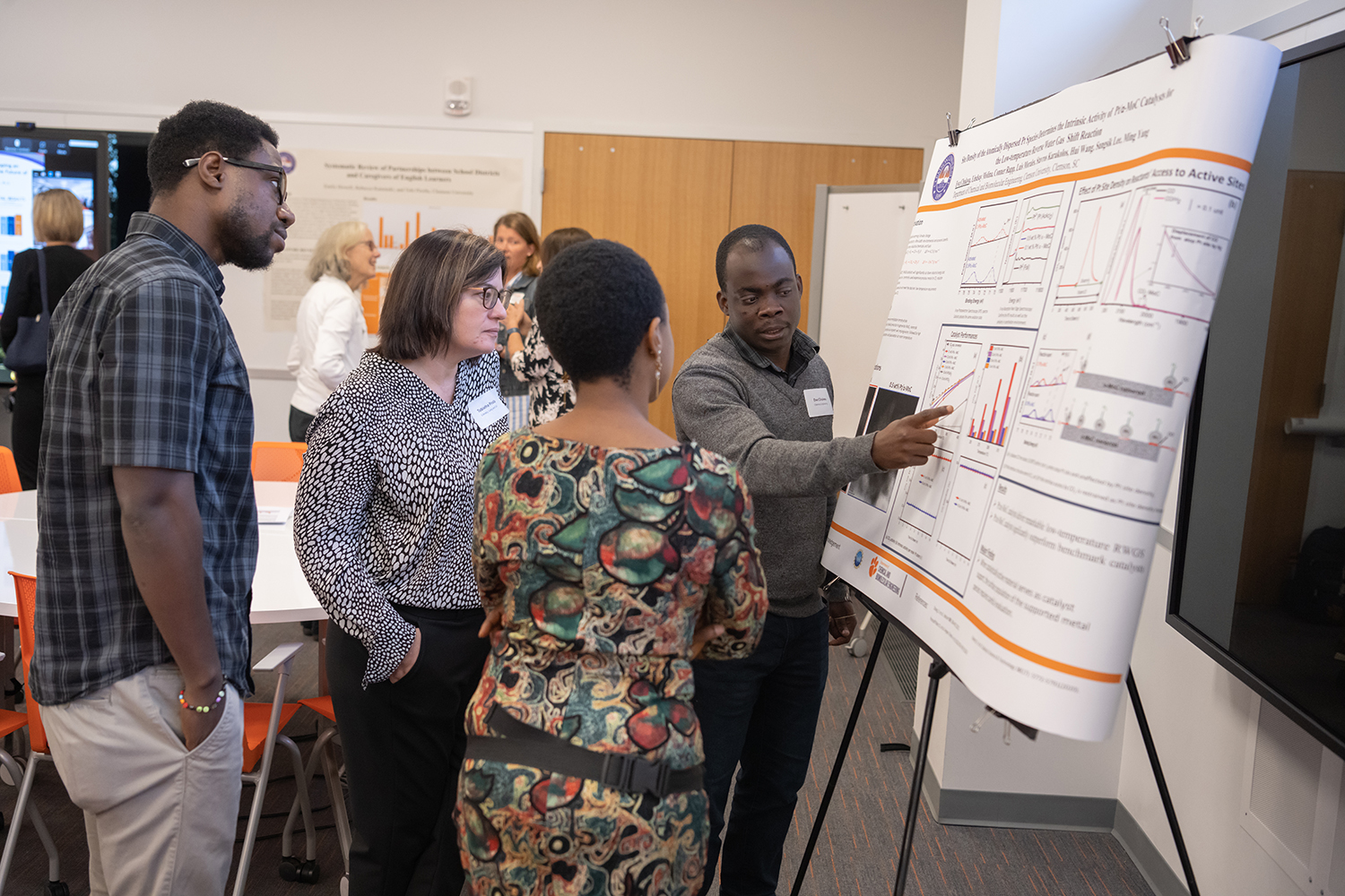 A man points to a research poster as three people watch