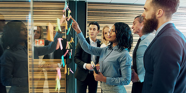 A group of professionals collaboratively brainstorming and discussing ideas using color-coded notes on a glass wall.