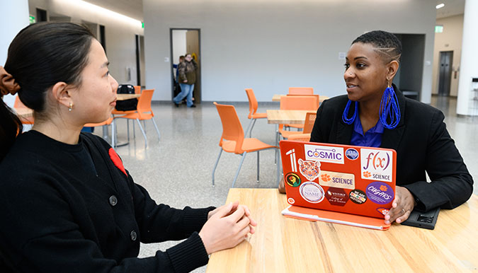 A mentor and student sit across from each other at a table while having a conversation.