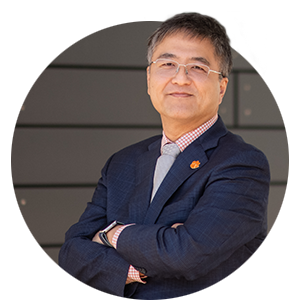 Dr. K.C. Wang stands with his arms crossed with an Orange Clemson Tiger paw pin on the label of his jacket.