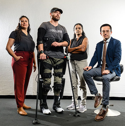 A group of four individuals, including a person in an exoskeleton, standing together with two women and a man in a suit.