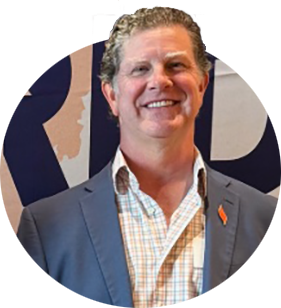 Craig Kinley wearing a gray blazer with an orange tiger paw pin on the lapel.