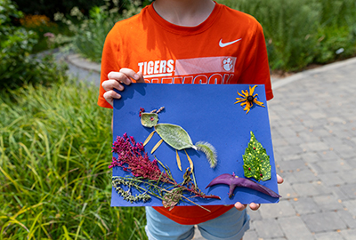child holding artwork from natural items collected from the garden