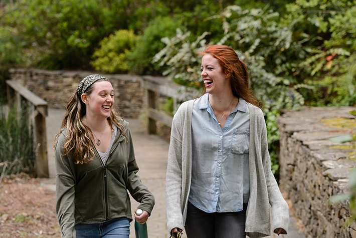 two girls share a laugh while walking through the garden