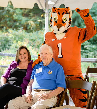 woman and man smiling with the Clemson tiger at a garden event
