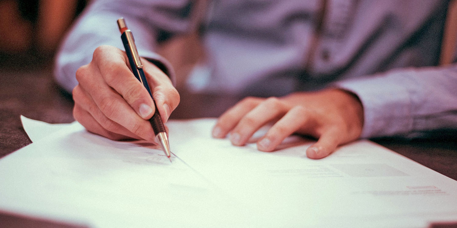 Decorative image of man's hands on paperwork with pen.