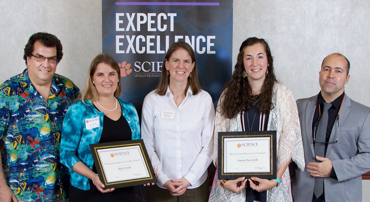 Five people, two holding awards. Three faculty members and two students.