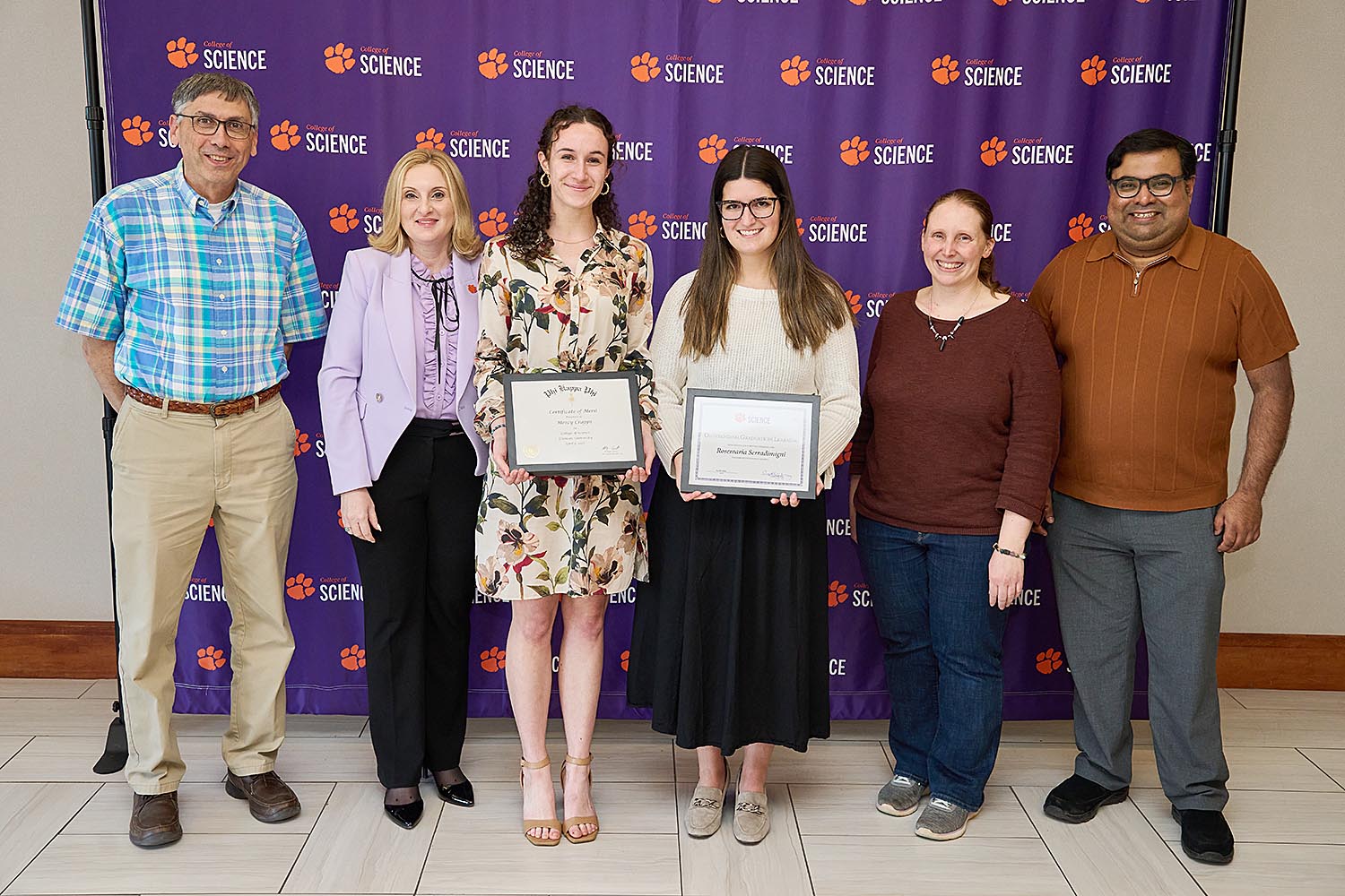 A group of six peple standing in front of a purple banner with the College of Science logo stepped and repeated across it.