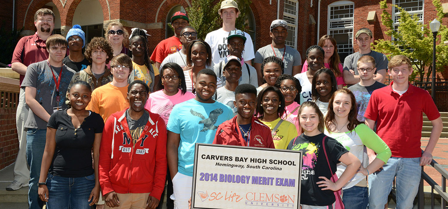 Group of high school students holding a sign for the 2014 Biology Merit Exam.