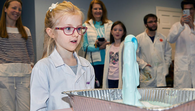 Young girl looking at blue foaming chemistry experiment.