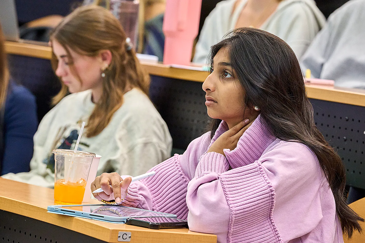 Female student in lecuture hall taking notes on a tablet.
