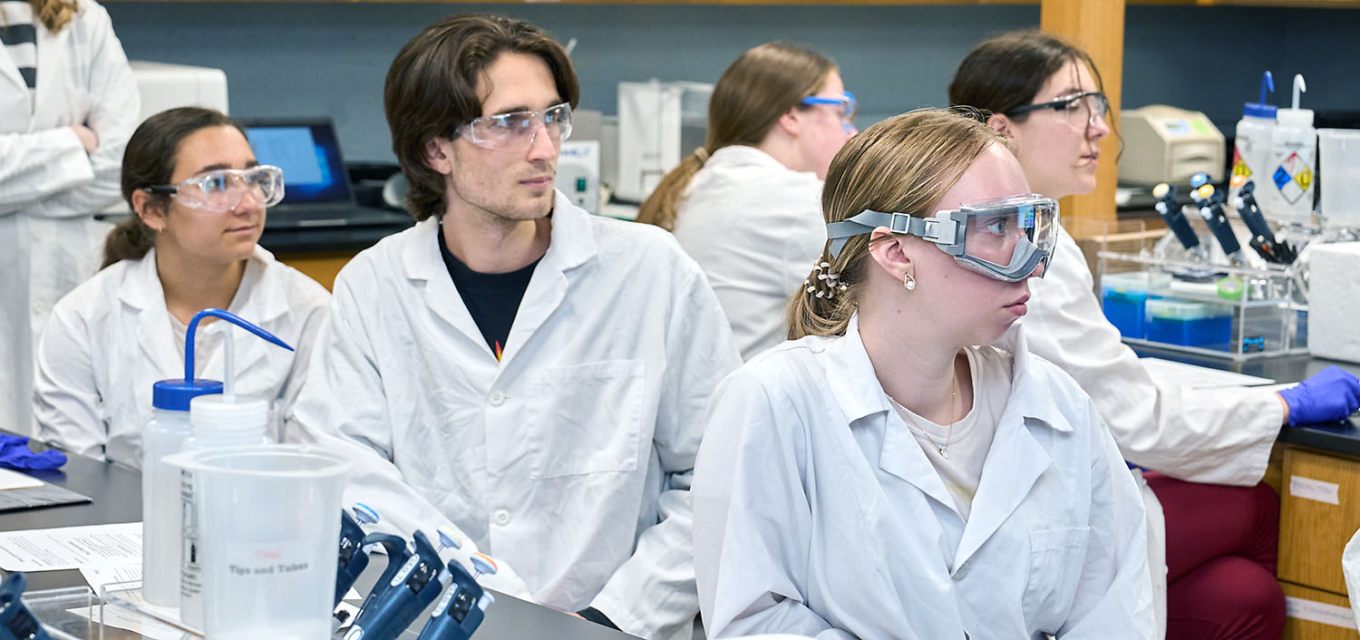 Studentswearing goggles in a lab at a lab table.