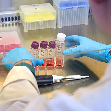 Colorful vials in a lab vent hood with a hand arranging them.