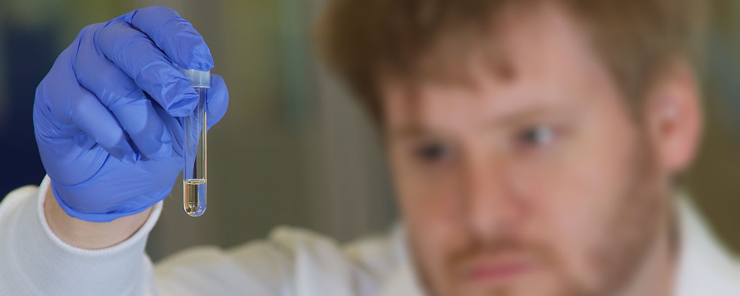 Vial of liquid being held in a hand, with head of male researcher blurred out.