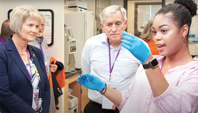 Student in lab showing two guests, a woman and man, an example of an experiment. 