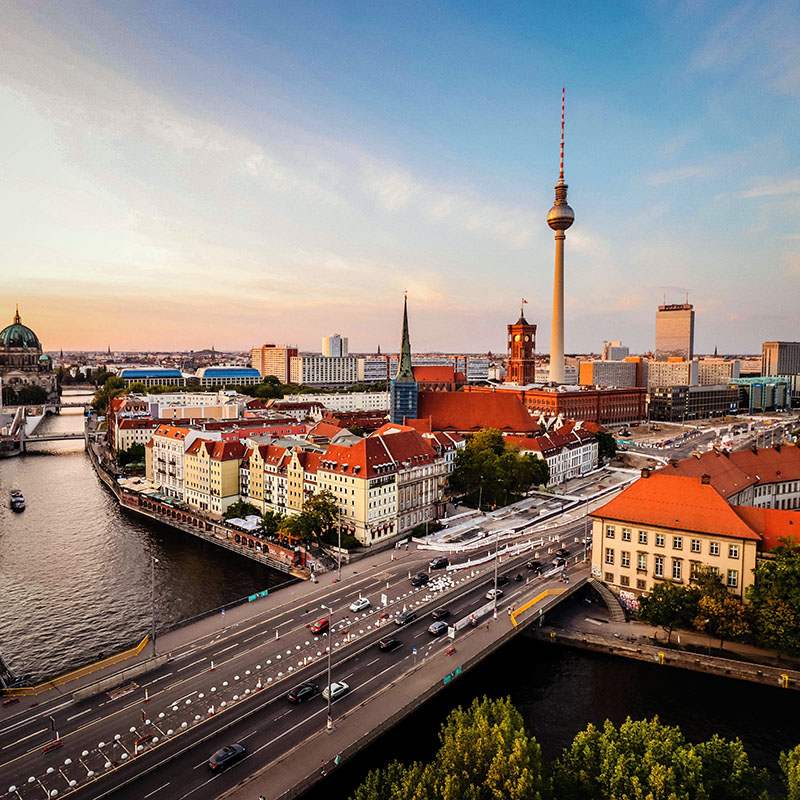 Aerial image of a city, Berlin, with buildings, many yellow and red-roofed, next to river.