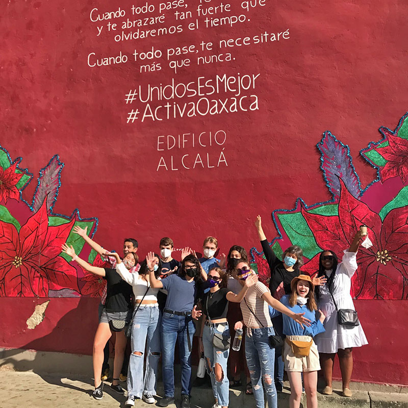Students in front of a red wall mural with text on it.