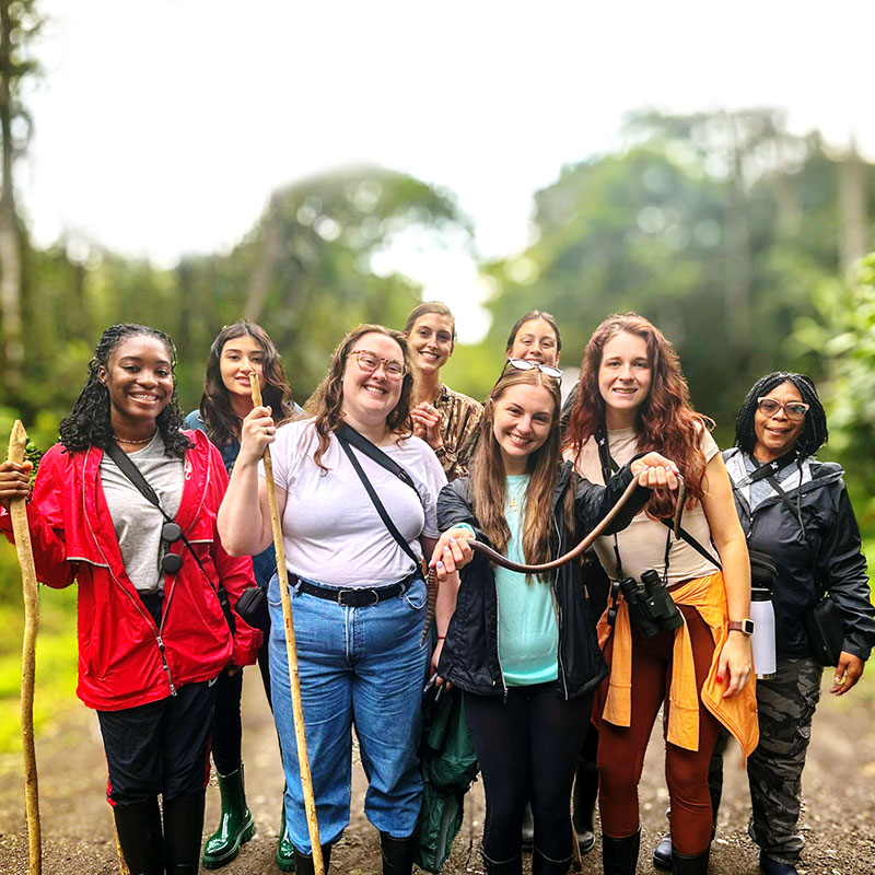 Group of eight people hiking in woods, one holding a snake in her hands.
