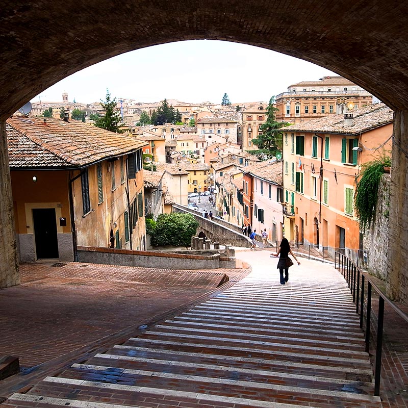 Person walking down steep, wide stairs outside in Italian city, surrounded by buildings.
