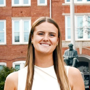 Headshot of woman, Amanda Geissler, in front of building and statue of man sitting.