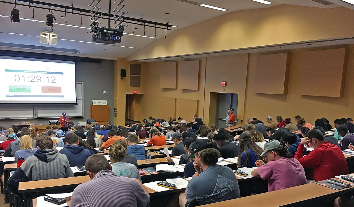 Students in auditorium taking a test, with a timer visible displaying 1:29:12.