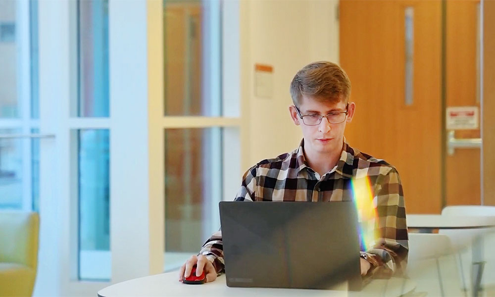 Man, Brandon Lumsden, working at computer on table in bright room.